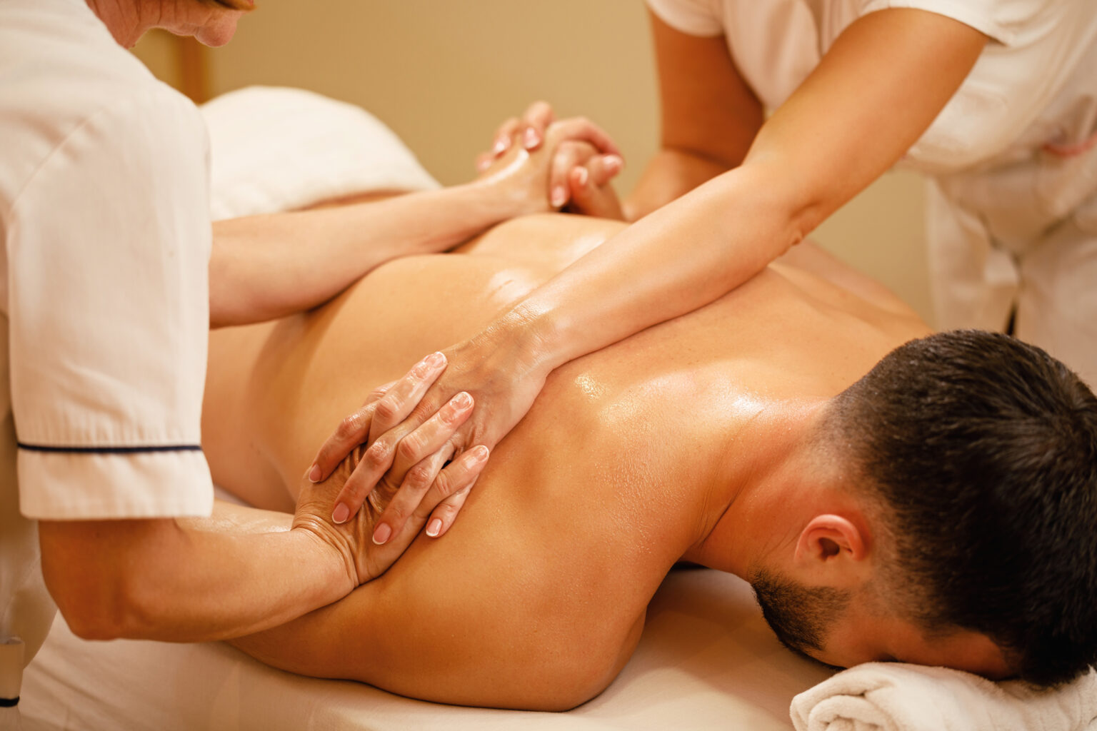 Unrecognizable massage therapists massaging together man's back at health spa.